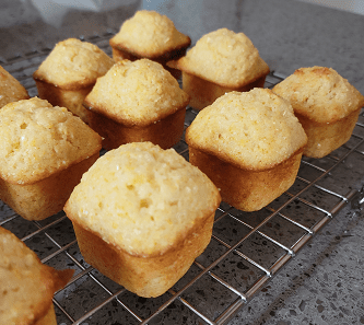Golden-brown mini corn muffins cooling on a wire rack, showcasing a fluffy texture and inviting appearance, ideal for serving as a snack or breakfast item.